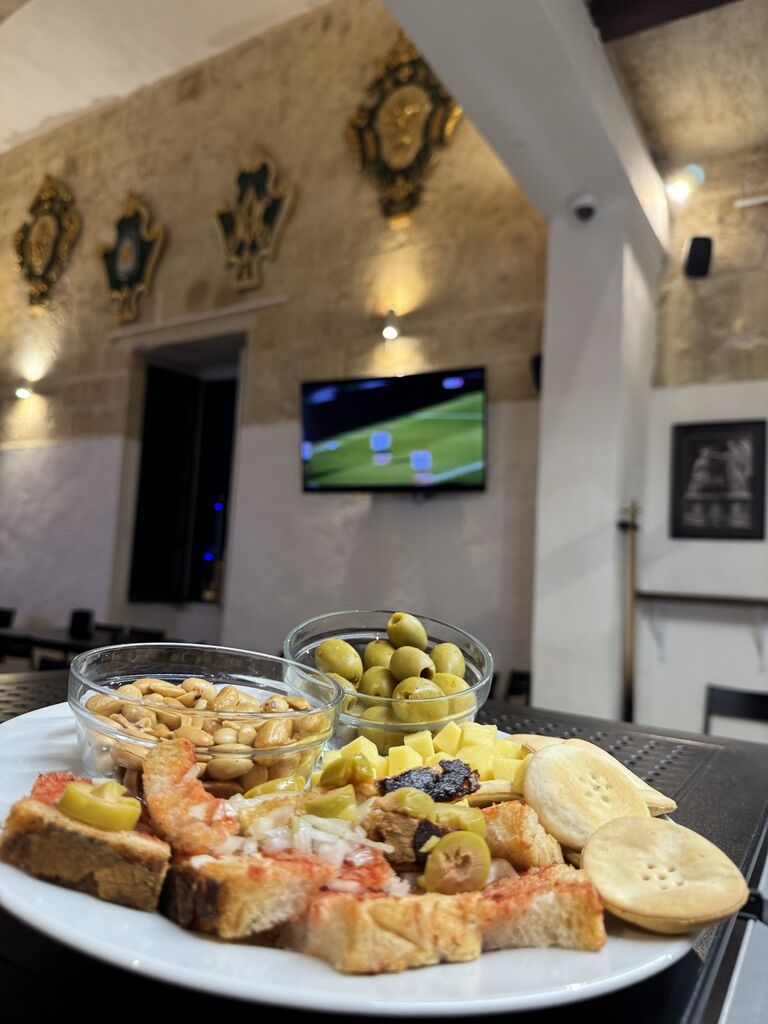 Platter of olives, peanuts, cheese and galletti with a football match on the TV behind