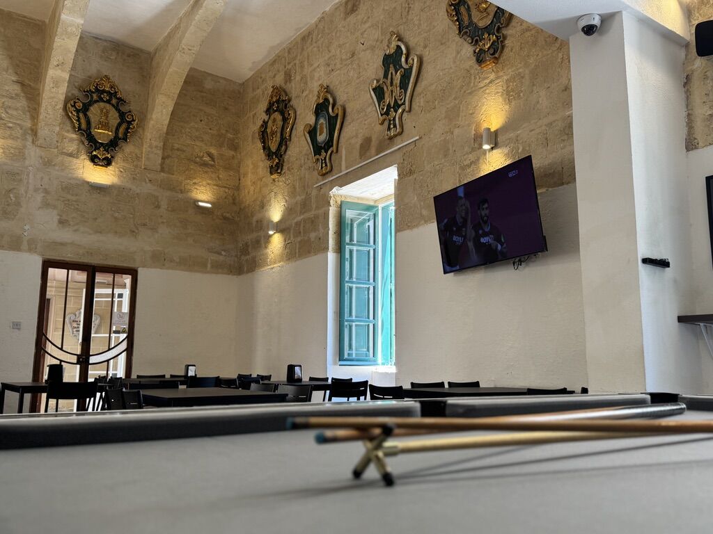 Pool table with cues in front of the hall, a TV showing a match on the wall